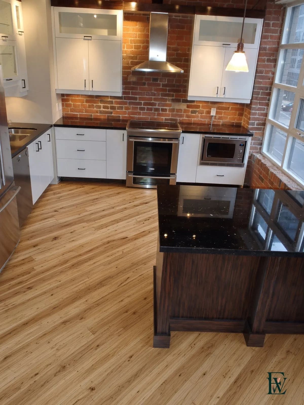 Character-grade light strip oak floor in a brick loft kitchen beside a granite island, frame 1 of 3, standing room view, Ecowoods site work, Toronto.