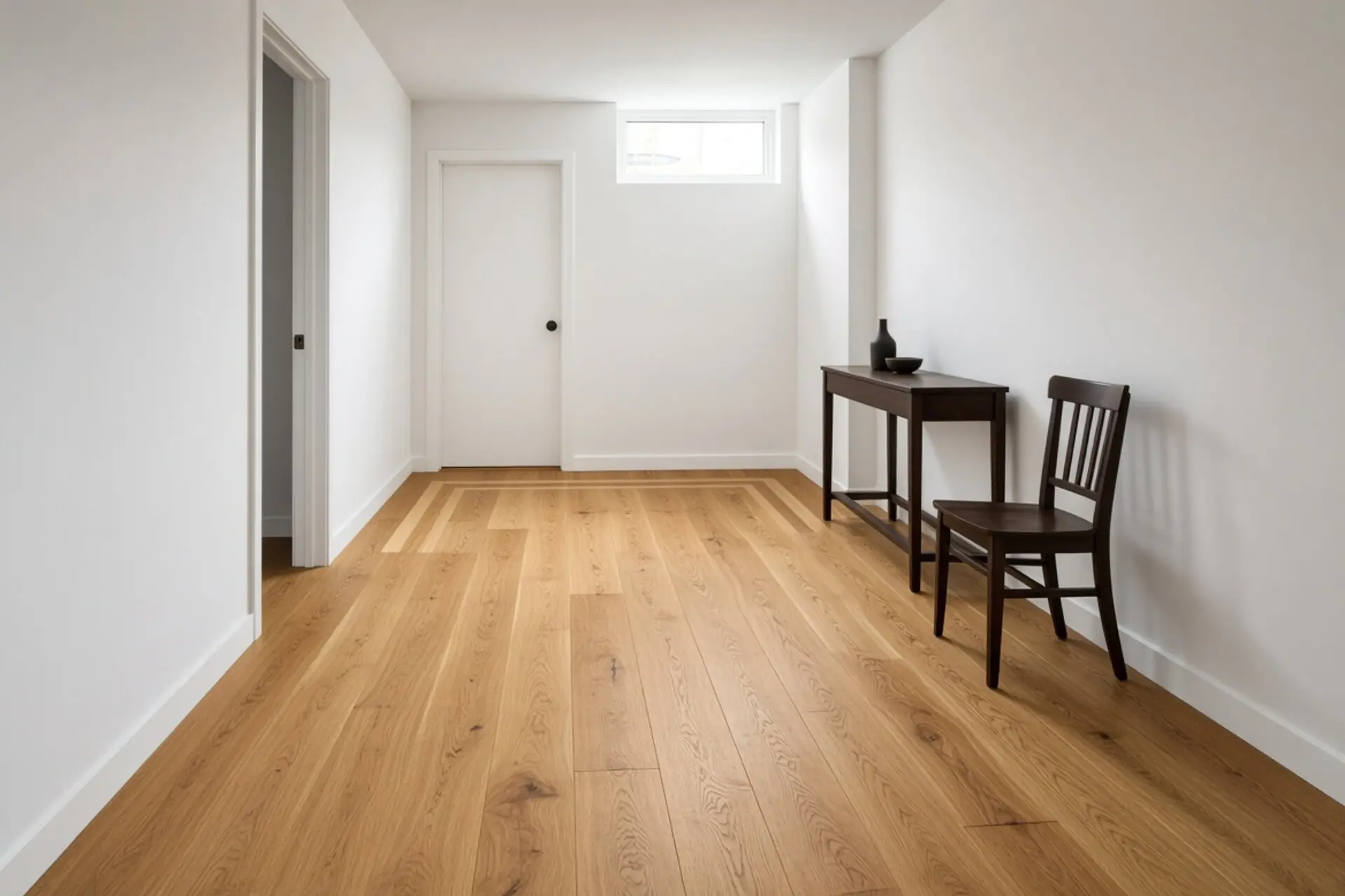 The same below-grade room after engineered hardwood: red oak field with hard-maple accent stripes, satin finish.