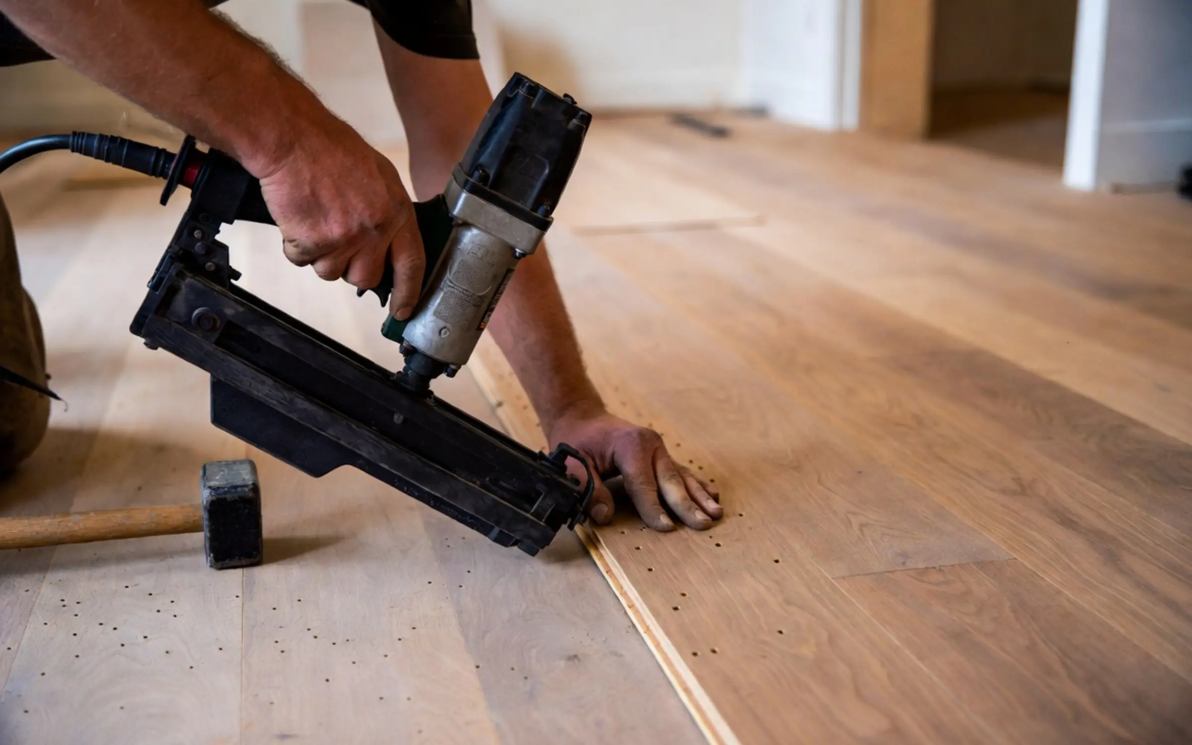 Craftsman using a pneumatic flooring nailer and mallet on hardwood planks