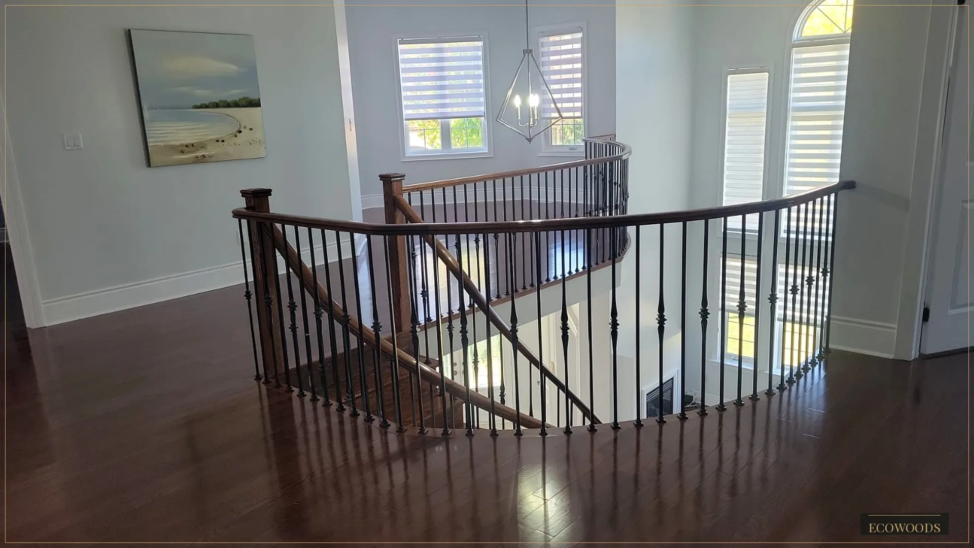 The upper landing after staining. The floor now reads deep and warm, the curved handrail matching, the black spindles unchanged.